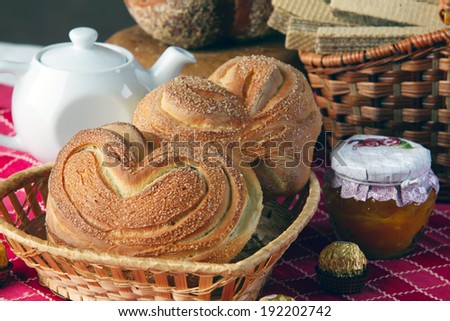 close-up of two sweet biscuits in the shape of hearts in the basket on red tablecloth and other pastries in the studio on a brown background