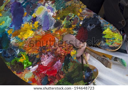 macro artist palette in hand, texture mixed oil paints in different colors and saturation studio
