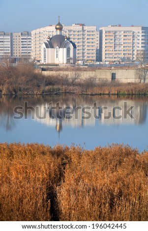 autumn landscape white stone church on the bank of the river on a background of a multistory building