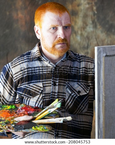 close-up portrait of an adult male artist with red hair and a beard at work studio on dark background