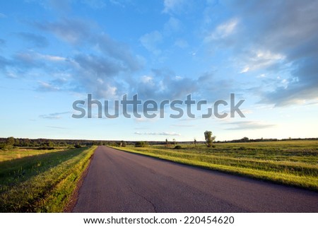 summer landscape road to the horizon at sunset and dramatic clouds on a blue sky