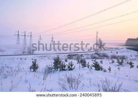 winter landscape railway tracks and power lines in the snow-covered field near the forest foggy morning
