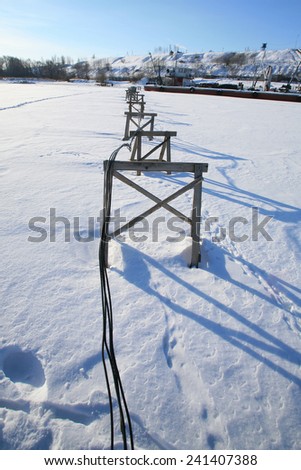 winter landscape river port, wooden supports for the cable on the ice river on a sunny day