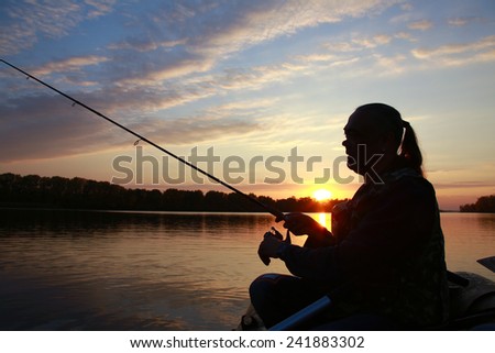 Portrait of a man in profile in a boat on a river with a fishing pole in his hands at sunset in autumn