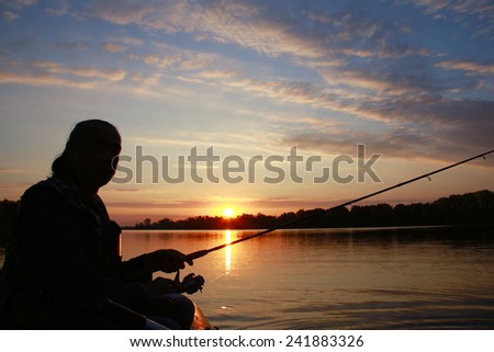 Portrait of a man in profile in a boat on a river with a fishing pole in his hands at sunset in autumn