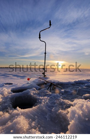 close-up drill, fishing rod near the hole on the ice in winter river at sunset