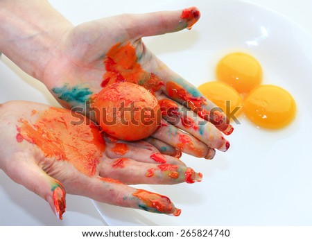 close-up of a single egg in the orange paint in female hands on a light background studio