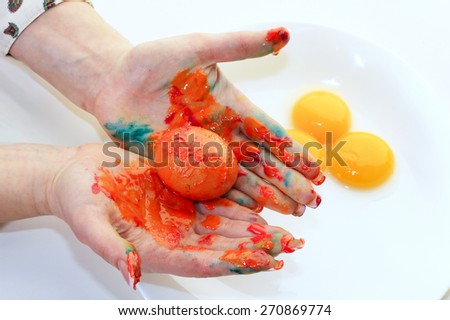 close-up of a single egg in the orange paint in female hands on a light background studio