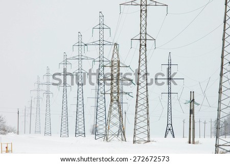 Winter industrial landscape high-voltage lines in the snow-covered field near the forest