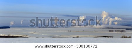 panorama of snow-covered fields and smoke from the chimneys of the plant on the horizon frosty misty morning