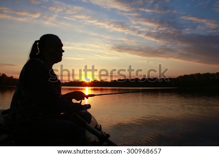 Portrait of a man in profile in a boat on a river with a fishing pole in his hands at sunset in autumn