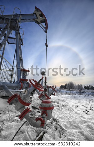 closeup of an oil pump in a snowy field near a forest in the sunlight halo