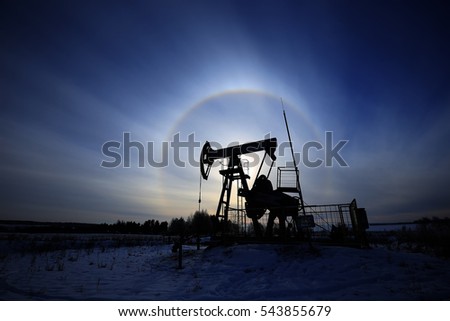 closeup of an oil pump in a snowy field near a forest in the sunlight halo