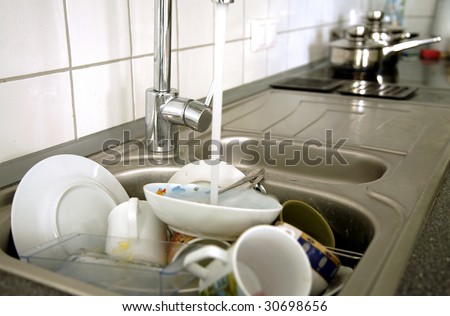 Pile of dirty dishes in the metal sink and pouring tap water. Kitchen after breakfast.