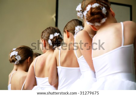 Little ballerinas dancing on a school show. Schoolgirls dressed in white dresses ( tutu ) with a daisy in their hair.