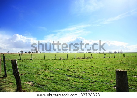 Green pasture in Le Nord enclosed with barbed wire fence. Intensive green and the sky with billowy clouds(cumulus ). Computer manipulation. France.