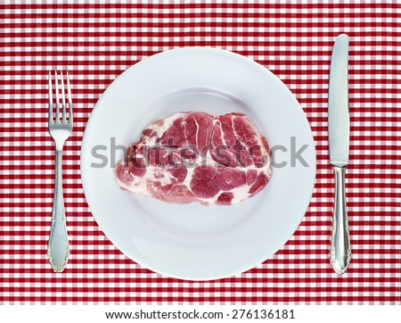 raw piece of meat on a plate with knife and fork