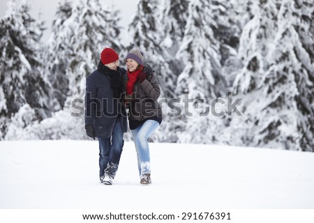 Couple walking in the snow and laughing in front of a snowy winter forest