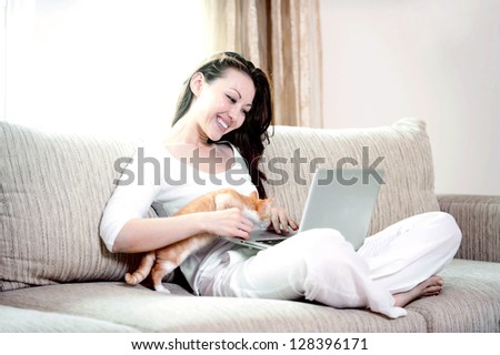 Attractive mixed asian woman with kitten on the couch using a laptop