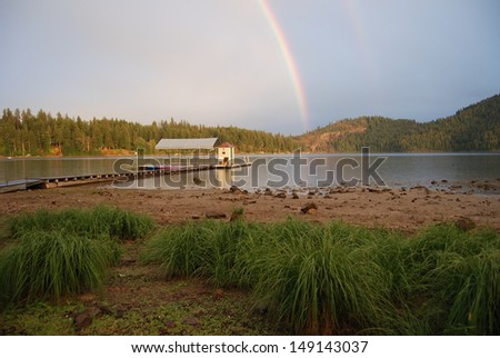 Rainbow over mountain lake with boat house.