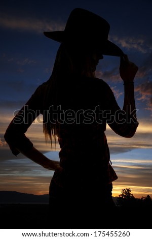 Silhouette of cowgirl tipping hat at sunset
