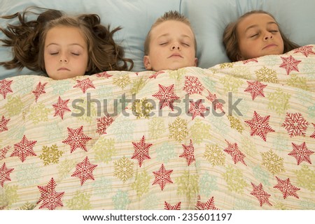 Boy and two girls asleep under blanket