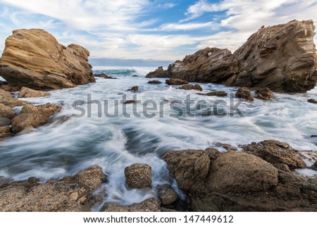 Rocky Seascape with blue sky, clouds and waves. This is an image of a rocky coastal scene with a blue cloudy sky and waves in the foreground.  This photo was taken in Laguna Beach, California.