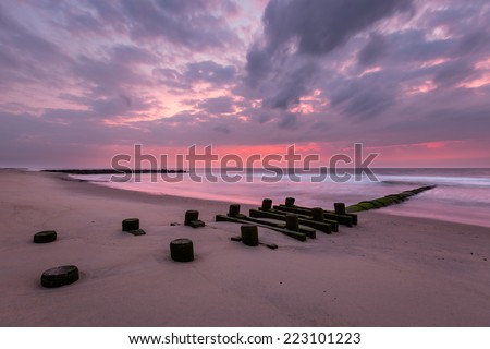 Seascape with storm drain and red dramatic sky.  This is a seascape image taken at sunrise of a storm drain at a beach with a dramatic red sky in the background