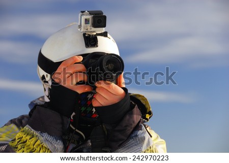 Snowboarder with action camera on helmet and SLR camera in his hands