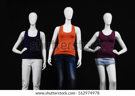 Row of three mannequin female dressed in colorful shirt and trousers on black background