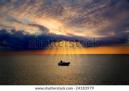 Lonely boat floating in sea is lit by divine light from dark cloud during sunset
