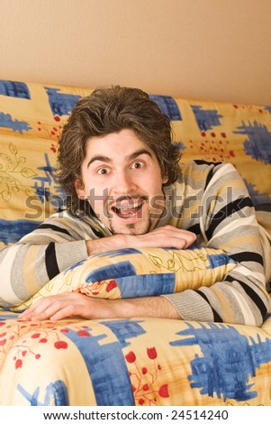 Young dark haired caucasian man in striped sweater lying on country style sofa and laughing