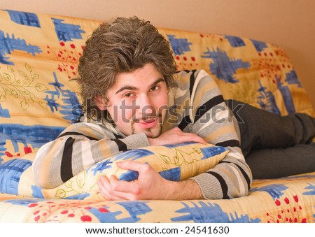 Young smiley dark haired caucasian man in striped sweater lying on country style sofa