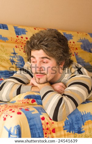 Young smiley dark haired caucasian man in striped sweater lying on country style sofa