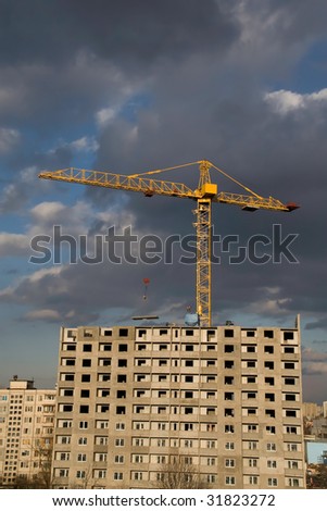 Hoisting crane lifting a concrete slab on a house being built, on the background of gloomy thunder clouds