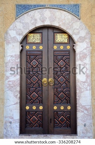 Sarajevo, Bosnia - March 23, 2015: Wooden door decorated with traditional Islamic geometrical designs and beautiful calligraphy on a mosque. The arched doorway is surrounded by white border and tiles.