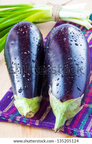 Two fresh eggplant with drops of water and a bunch of green spring onions on towel