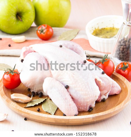Raw whole small chicken with black pepper and herbs on wooden plate on kitchen table