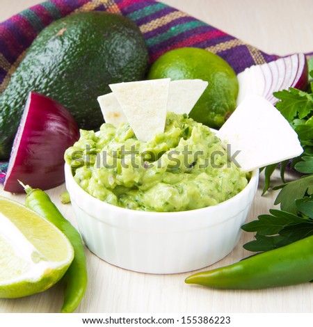 Green Mexican guacamole dip with avocado, lime, parsley and red onions in white Ã?Â?Ã?Â�up and vegetables around