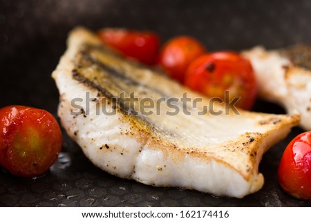 White fish fillet of perch, cod with tomato on fried pan