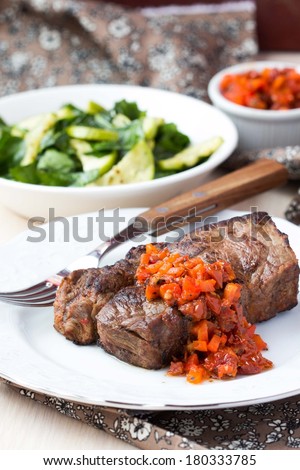 Grilled beef steak with salsa sauce made from sun-dried tomatoes, red peppers and green zucchini salad with spinach, delicious dinner