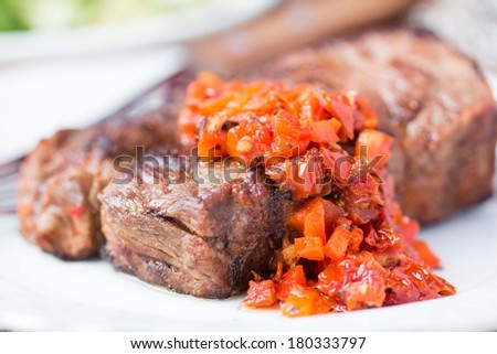 Grilled beef steak with salsa sauce made from sun-dried tomatoes, red peppers and green zucchini salad with spinach, delicious dinner