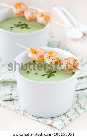 Velvety green cream soup of broccoli, peas, spinach, fried shrimps on sticks in two white bowls