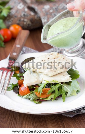 Fried white fish fillet with salad of lettuce, arugula, greens, tomatoes, green sauce with pea, parsley