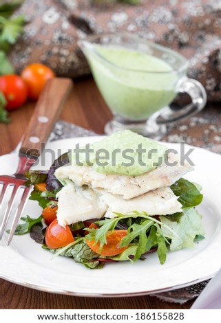 Fried white fish fillet with salad of lettuce, arugula, greens, tomatoes, green sauce with pea, parsley