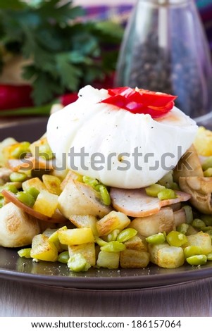 Hot appetizer salad with potatoes, ham, green peas, mushrooms, poached egg with resultant yolk