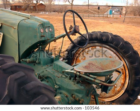 An old tractor in a field, showing the steering wheel, seat, and the large rear tires.