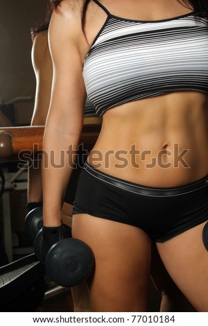 A close-up shot of the torso of a female dressed in fitness wear, holding a hand weight,facing the camera.