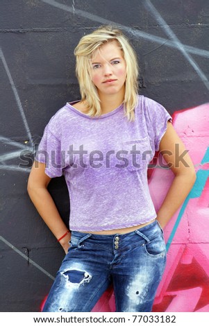 A lovely young blonde leans against a graffiti-covered wall.