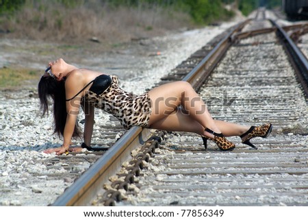 A lovely woman with auburn hair and wearing a tight leopard-print dress, relaxing in the sun on a railroad track.